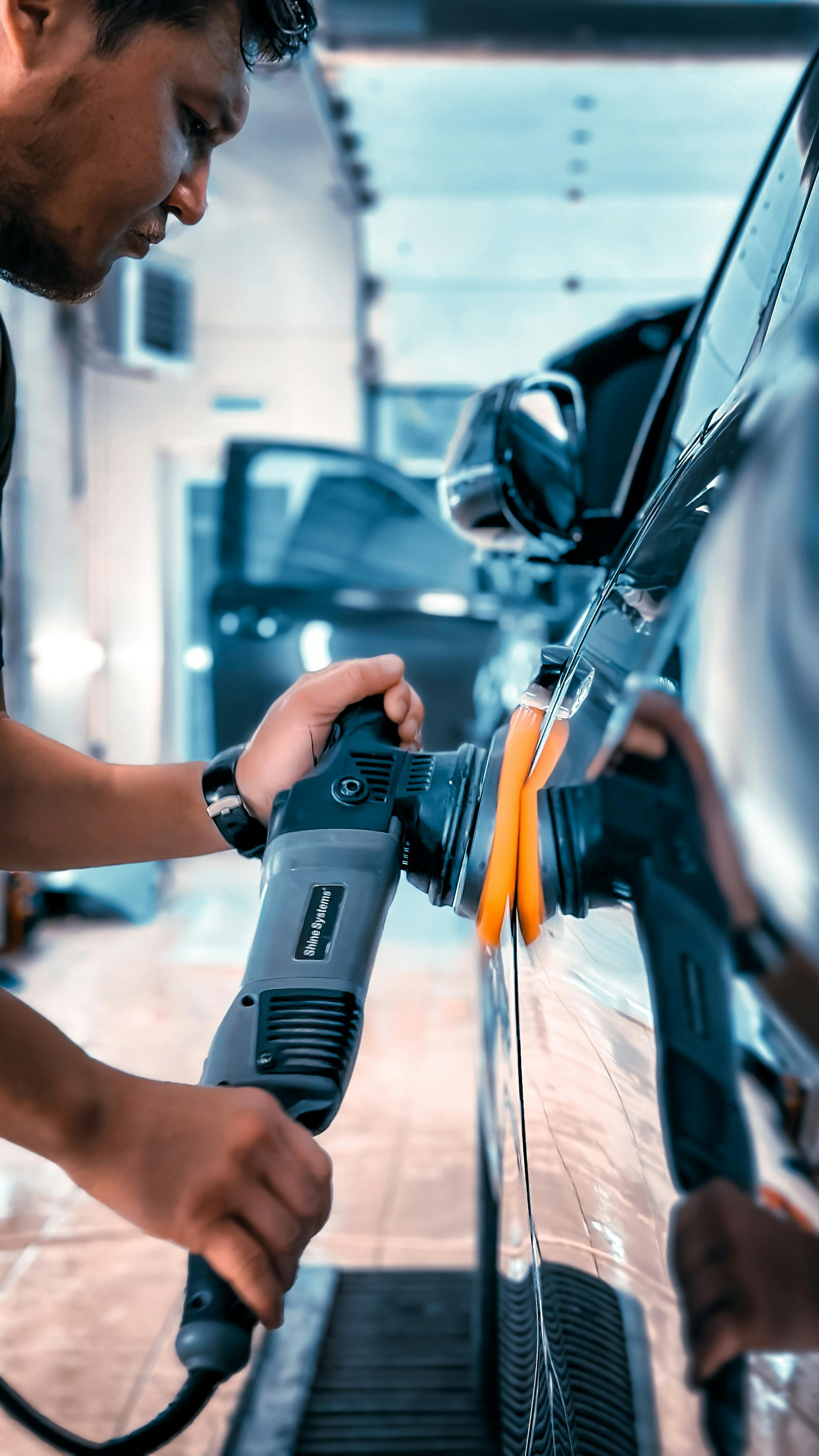 Meistras poliravimo mašinėle apdirba tamsaus automobilio šoninę dalį